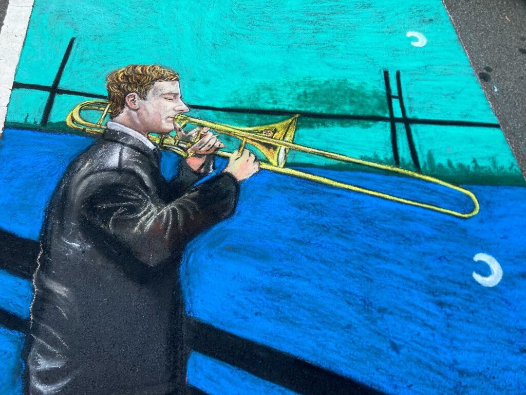 chalk art drawing of a musician playing trombone in front of a river